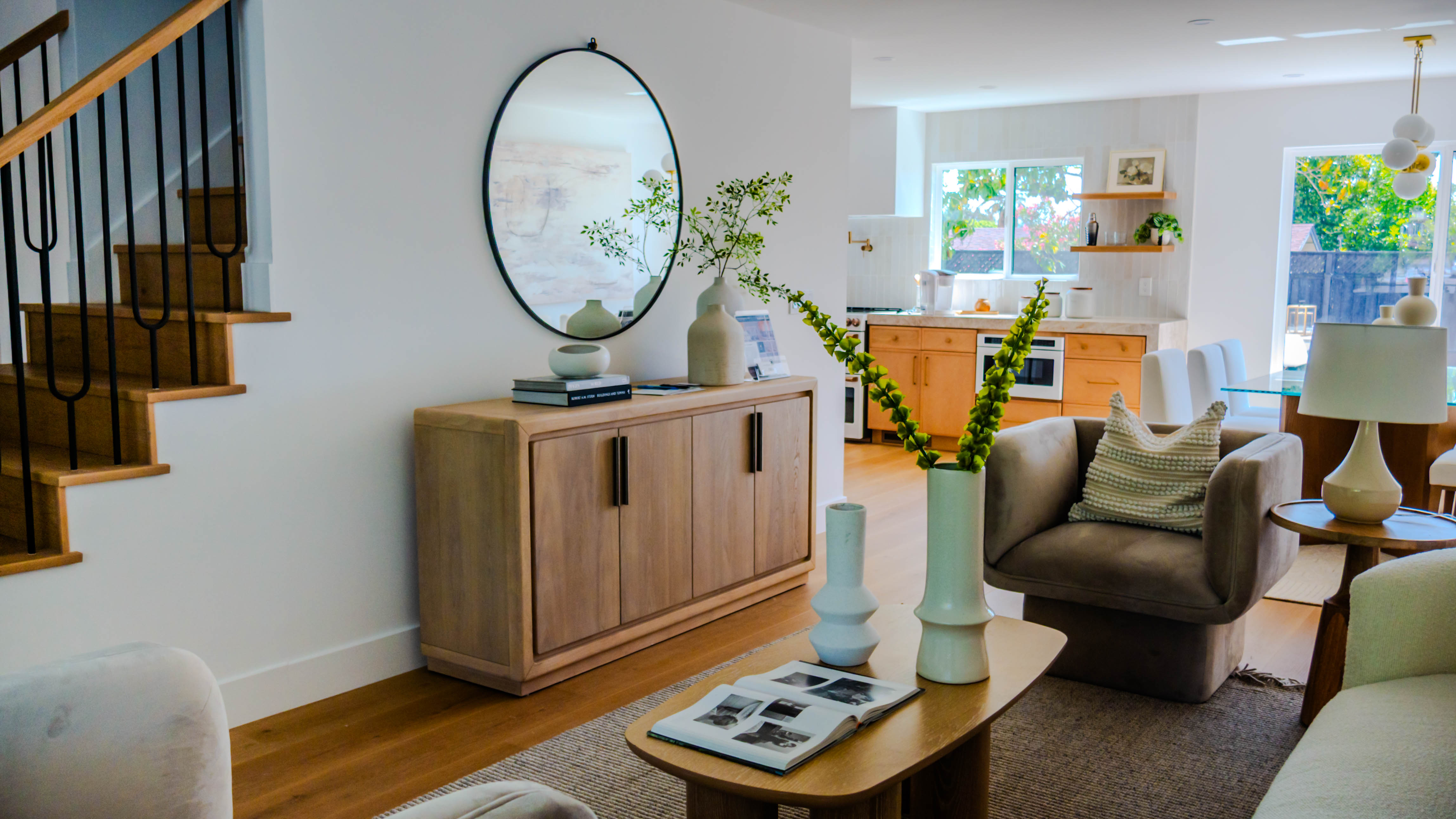 Living room with modern staircase featuring black metal railings, wooden credenza, and open flow to kitchen